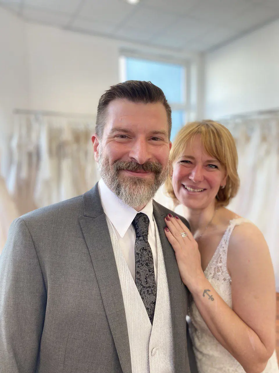 Glückliche Kundin nach dem Kauf ihres figurbetonten Brautkleids mit Spitze im Brautgeschäft, gemeinsam mit ihrem Mann. Perfekte Wahl für ihre zweite Hochzeit – traumhafte Brautmode in Essen, Düsseldorf und Velbert.