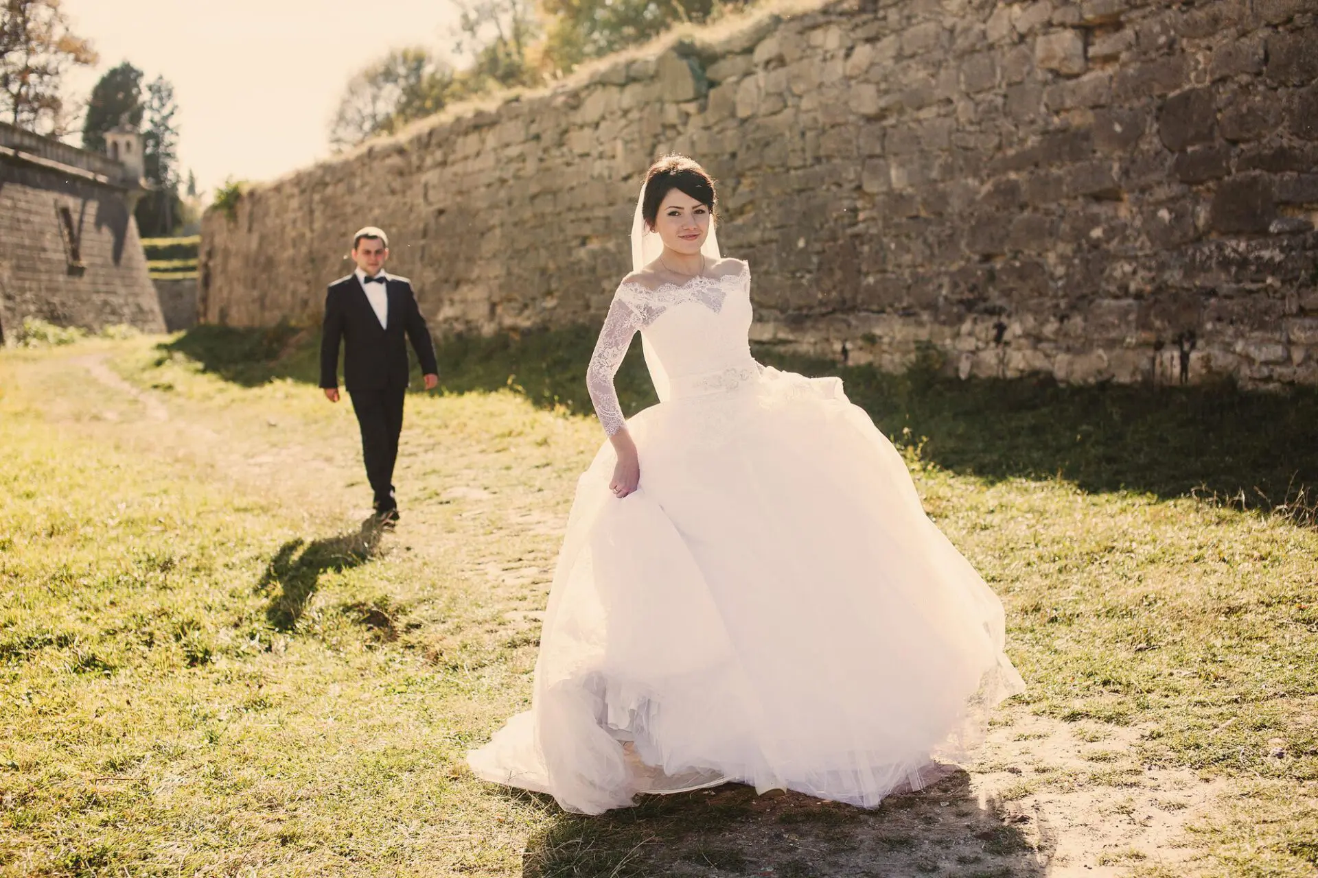 Braut in einem eleganten Prinzessinnen-Brautkleid mit langer Schleppe steht vor einem märchenhaften Schloss.