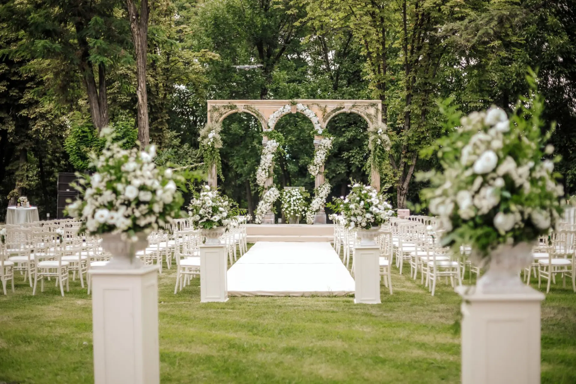Braut in einem Vintage-Spitzenkleid mit langen Ärmeln posiert in einer rustikalen Scheune mit Lichterketten.